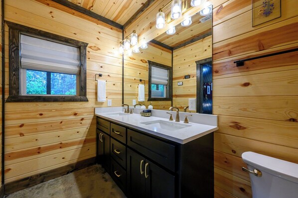 Une salle de bain rustique, avec une cabine en bois, comprenant un lavabo double, un meuble-lavabo, un miroir et des toilettes.