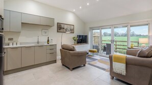A modern kitchen with a dining area, a sofa, and a view of a green field. - 1 bedroom accommodation in Clitheroe (Clitheroe)