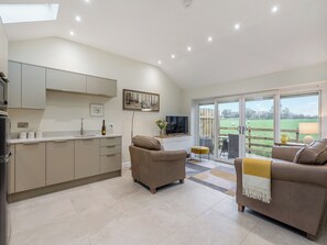 A modern kitchen with a dining area, a sofa, and a view of a green field.
