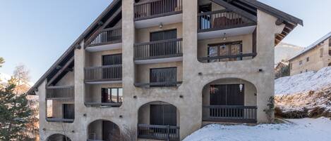 A multi-story building with balconies and arched doorways, surrounded by snow.