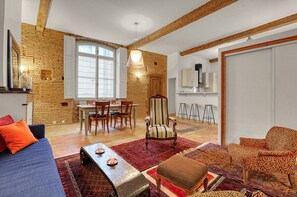Een ruime woonkamer met een eettafel, een gestreept fauteuil en een bank met kleurrijke kussens.