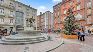 A public square with a central fountain, surrounded by historic buildings and a decorated Christmas tree. - L'Encrier - Appt confortable pour 2 (Toulouse)