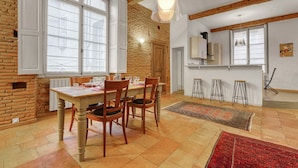 A dining area with a wooden table and chairs, a red rug, and a kitchen in the background. - L'Encrier - Appt confortable pour 2 (Toulouse)
