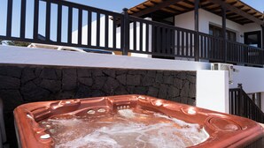 A hot tub with a stone wall backdrop, a balcony with a wooden railing, and a clear blue sky. - Casa Pari Luxury (Playa Blanca)