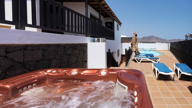 A hot tub with a stone wall, a pool with lounge chairs, and a view of mountains. - Casa Pari Luxury (Playa Blanca)