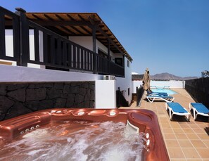 Un bain à remous avec un mur en pierre, une piscine avec des chaises longues et une vue sur les montagnes.