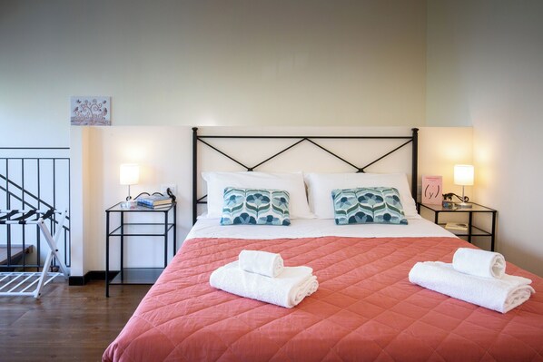 A neatly made bed with a pink quilt, white pillows, and two rolled towels. There are two bedside tables with lamps and a small decorative item on one. - Cozy loft with small pets allowed (Firenze)