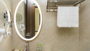 A bathroom with a large mirror, a towel rack with folded towels, and a sink with a faucet.