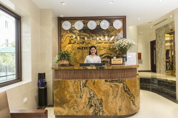 Mostrador de recepción de hotel con diseño de mármol, varios relojes y un recepcionista.
