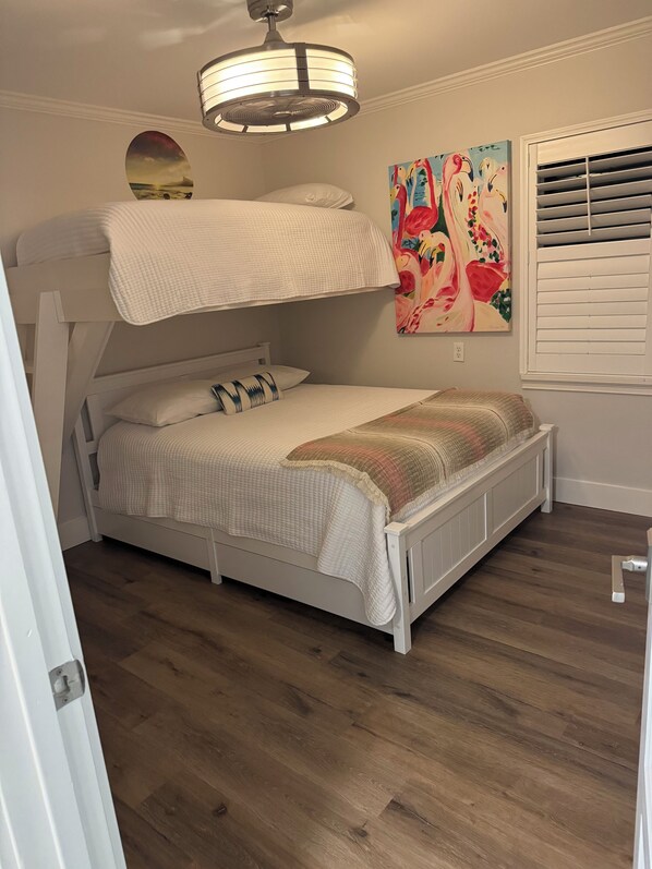 Una cama litera con ventilador de techo, un cuadro y una ventana con persianas.