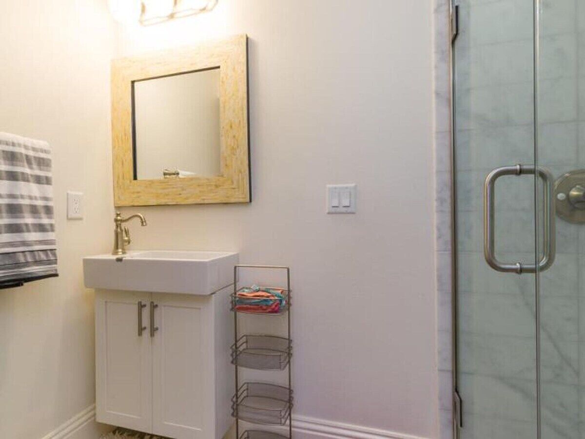 Une salle de bain avec un lavabo blanc, un miroir avec un cadre en bois, un porte-serviettes et une porte de douche en verre.