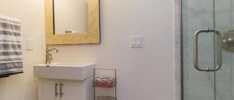 Une salle de bain avec un lavabo blanc, un miroir avec un cadre en bois, un porte-serviettes et une porte de douche en verre.