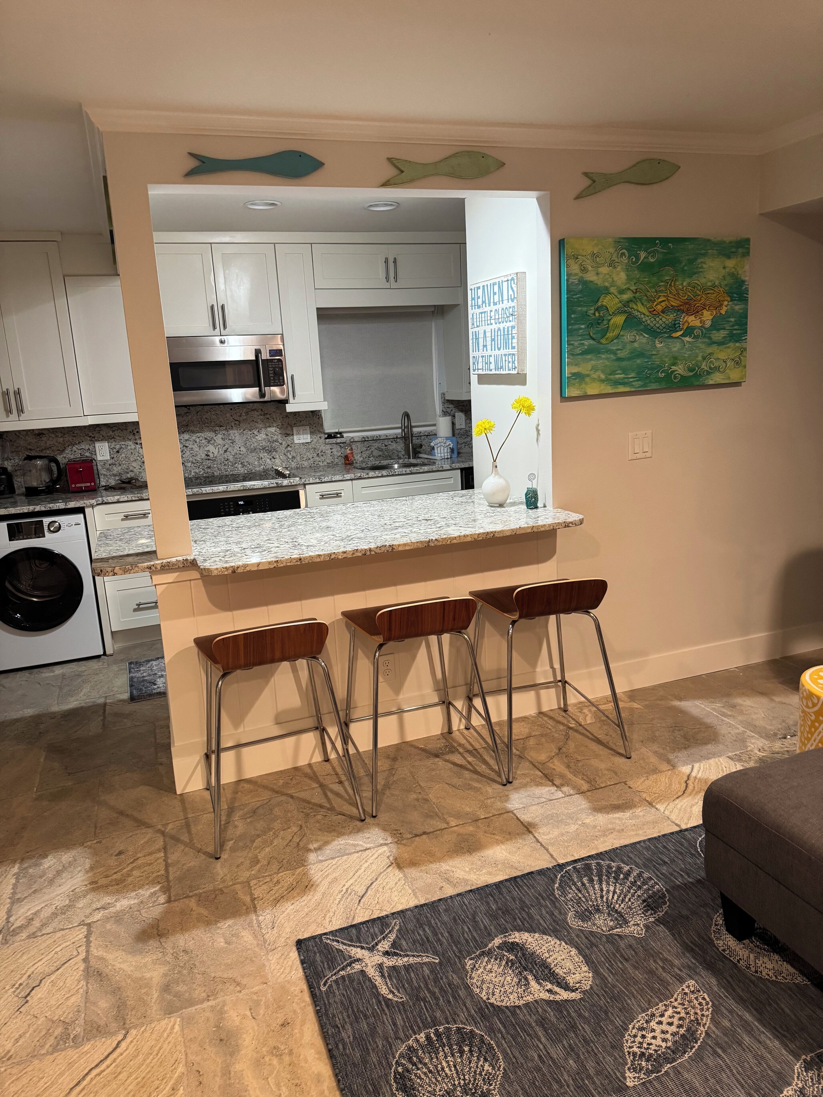 Een moderne keuken met een centraal eiland, barstoelen en een decoratief kunstwerk van vissen aan de muur.