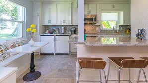 Une cuisine moderne avec des meubles blancs, un plan de travail en granit et un coin repas comprenant une table blanche et quatre chaises.