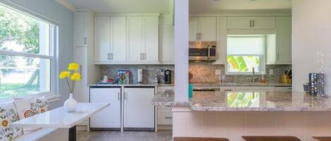 Una cocina moderna con armarios blancos, encimera de granito y comedor con una mesa blanca y cuatro sillas.
