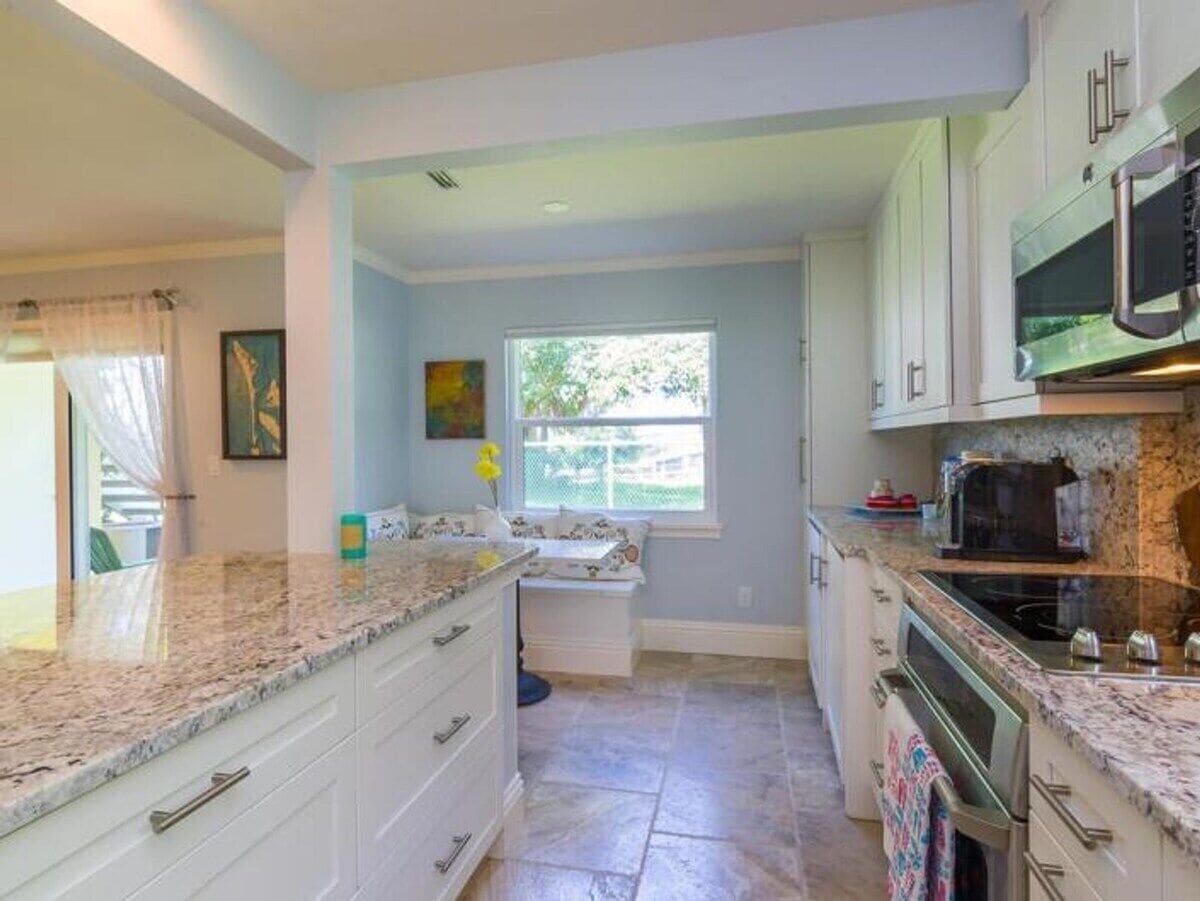 A kitchen with granite countertops, white cabinets, a built-in oven, and a window with a view of greenery.