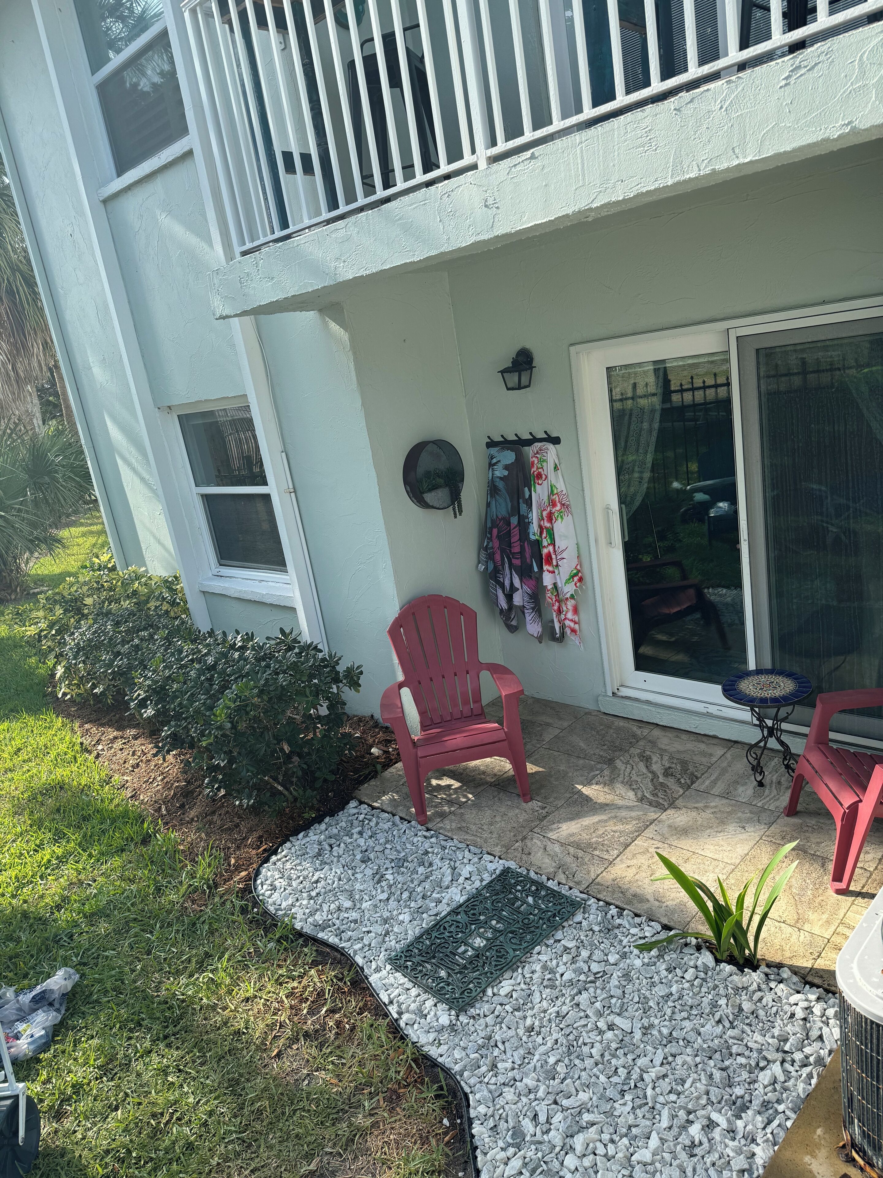 A patio with a red chair, a small table, and a decorative wall hanging.