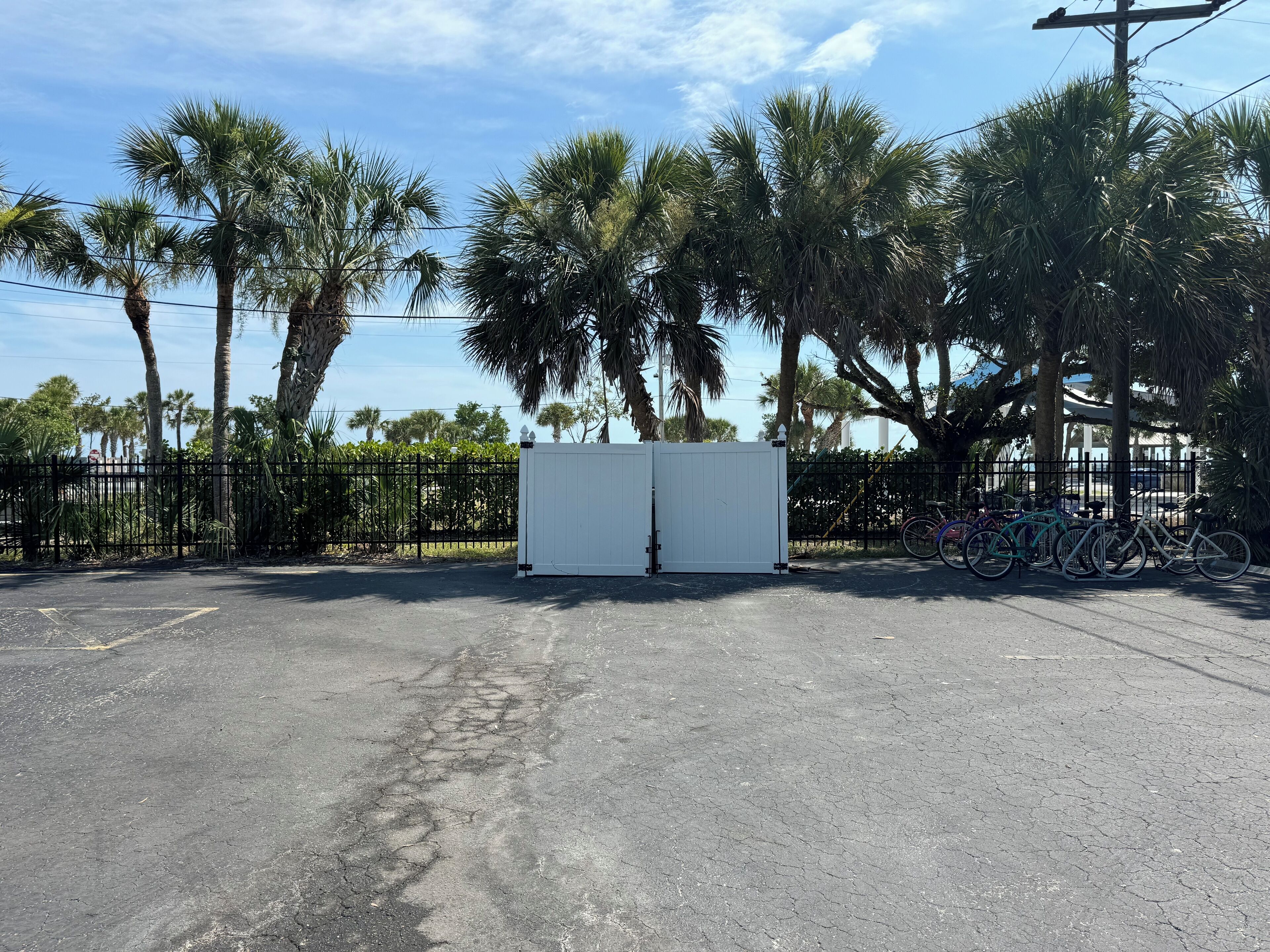 A gated parking area with a white container, surrounded by palm trees and a bicycle rack.