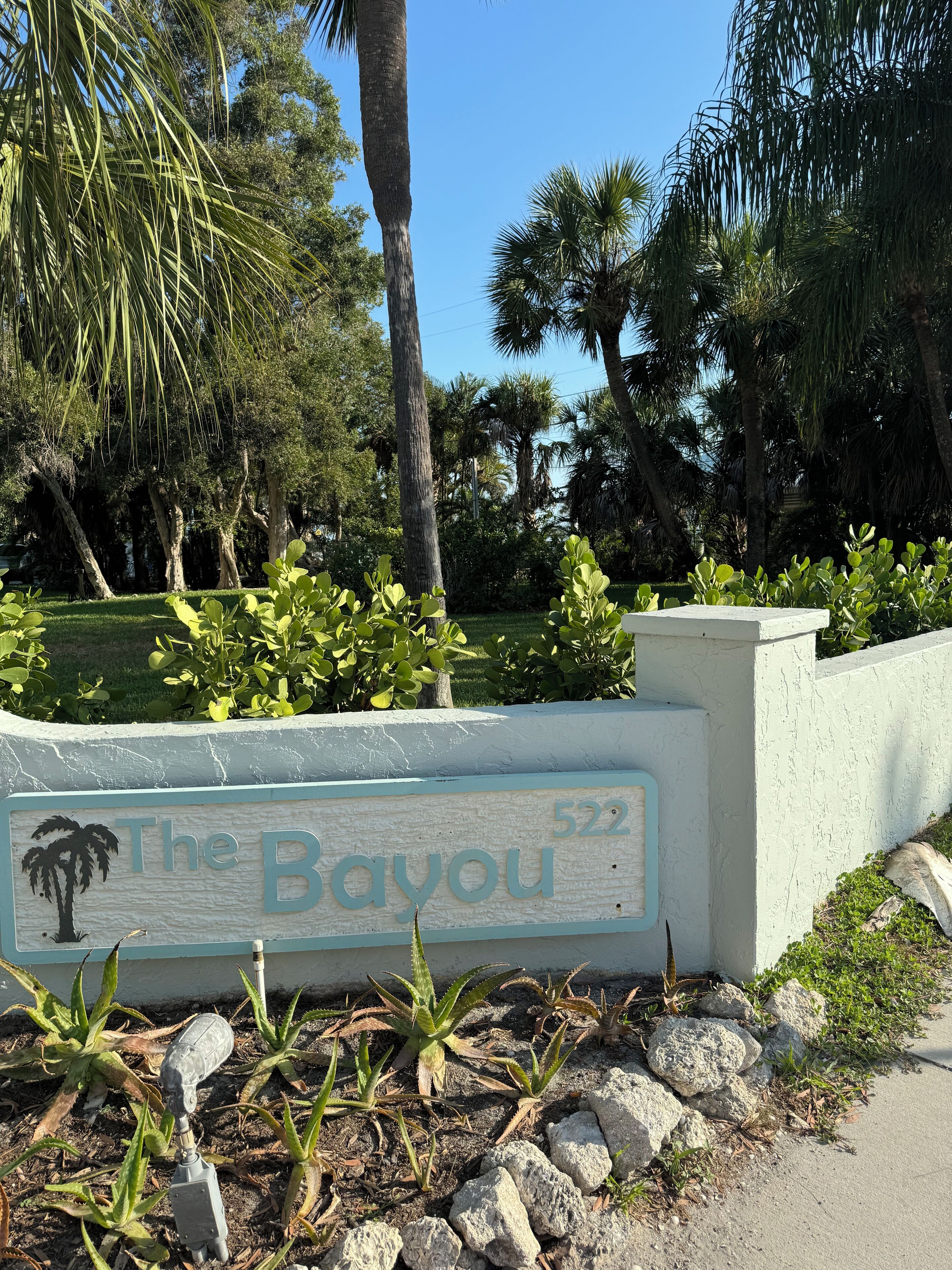 Een bord met 'The Bayou', met een palmboomafbeelding, omringd door begroeiing en rotsen.