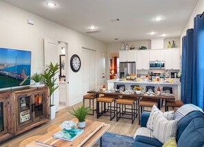 Une cuisine moderne avec des meubles blancs, un coin repas doté d’une table et de chaises en bois, et un salon avec un canapé bleu.