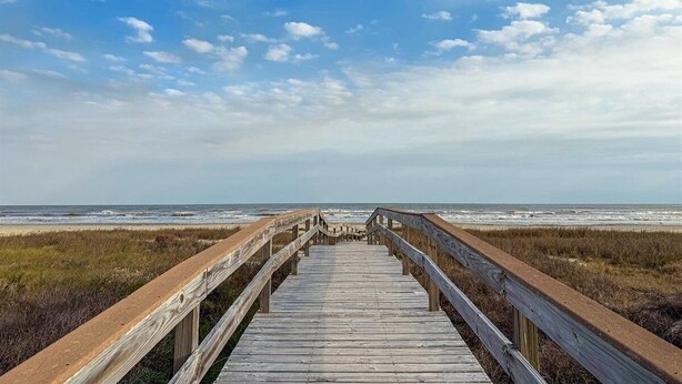 Ein hölzerner Steg führt zum Strand, der Himmel ist wolkenlos.