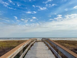 A wooden boardwalk leading to the beach with a clear sky. - Hot Tub | Beach View | Pet Friendly | 2 King Suite (Galveston)