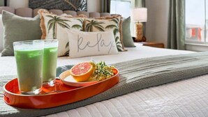 Ein Hotelzimmer mit Bett, Kissen, einem Tablett mit zwei Gläsern grünen Getränks, einem Teller mit einer Grapefruitspalte und Kräutern sowie einem Kissen mit dem Schriftzug 'Relax'.