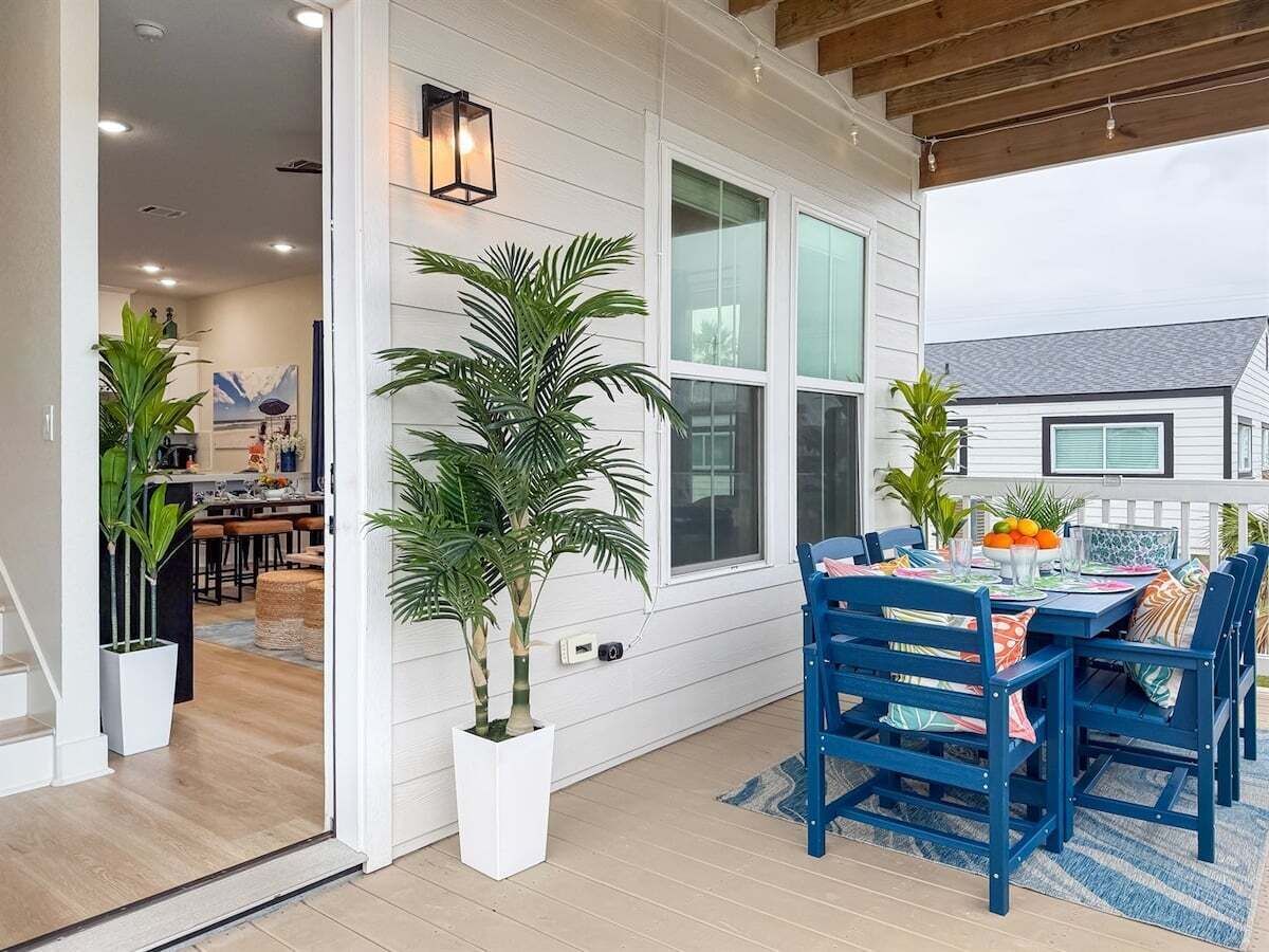 A covered patio with a dining table and chairs, potted plants, and a view of the house.