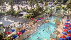 Ein Resort-Poolbereich mit mehreren Schwimmbecken, Liegestühlen, Sonnenschirmen und Palmen.