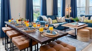 Ein modernes Wohnzimmer mit Essbereich, ausgestattet mit einer Sofagarnitur, einem Couchtisch und einem Esstisch mit Gläsern und einer Flasche.