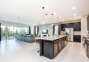 A modern kitchen with a central island, dark cabinetry, and a large window overlooking a pool.