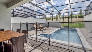 Un'area esterna coperta con piscina, poltrone relax e tavolo da pranzo.