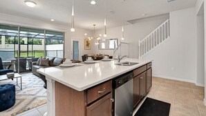Una cucina moderna con un'ampia isola, elettrodomestici in acciaio inossidabile e illuminazione a sospensione.