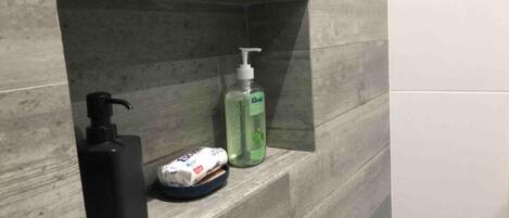 A bathroom shelf with a black soap dispenser, a green liquid soap bottle, and a small white package.