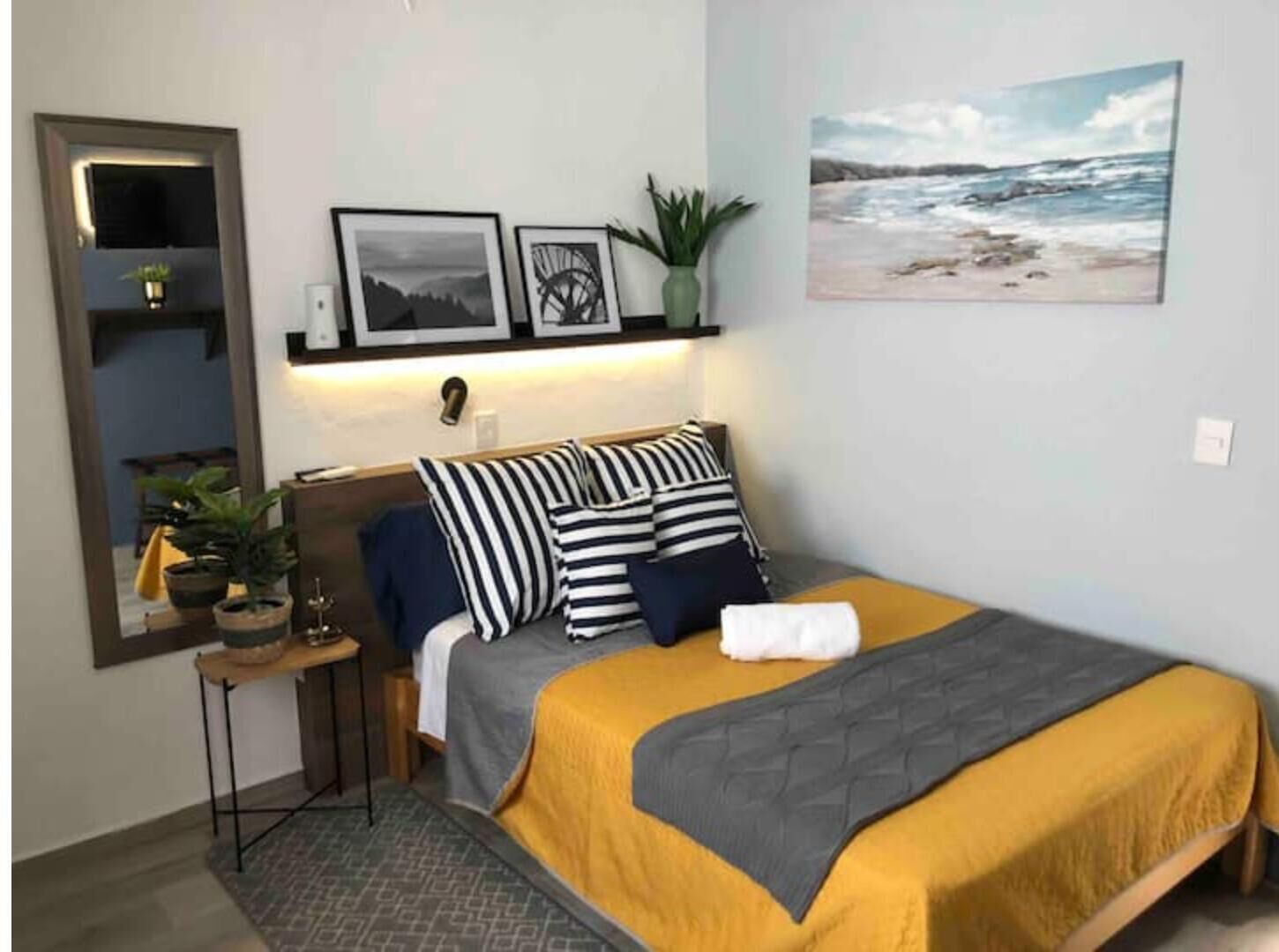 Een slaapkamer met een bed, nachtkastje, spiegel en wanddecoratie.