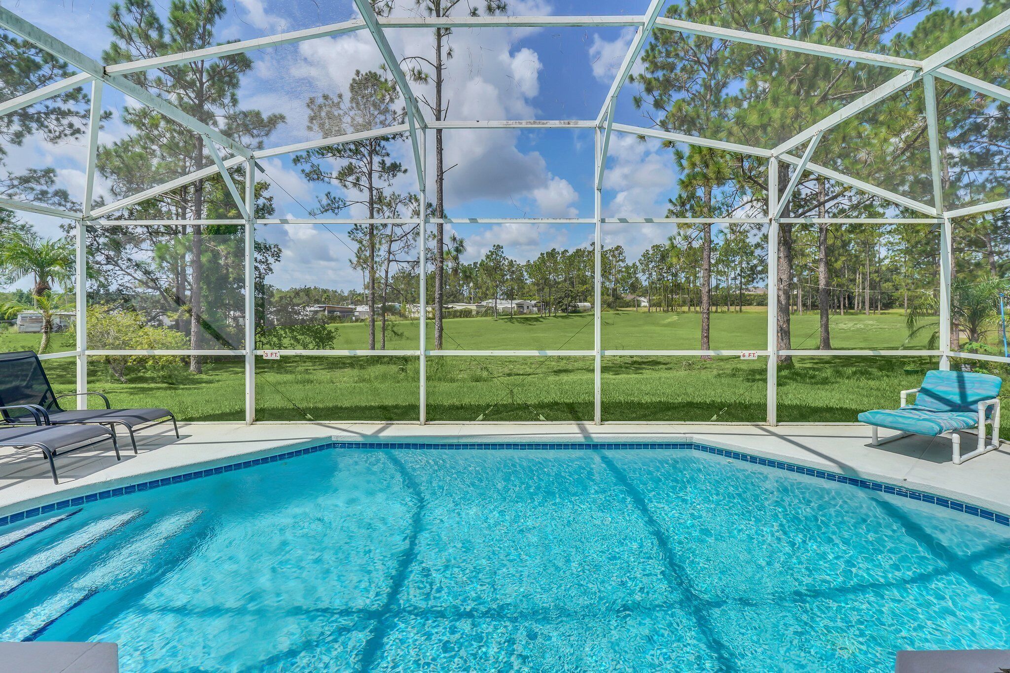 A swimming pool with a clear view of the surrounding landscape, including trees and a grassy area.