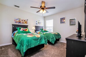 A bedroom with two beds, a ceiling fan, a desk, and a TV.