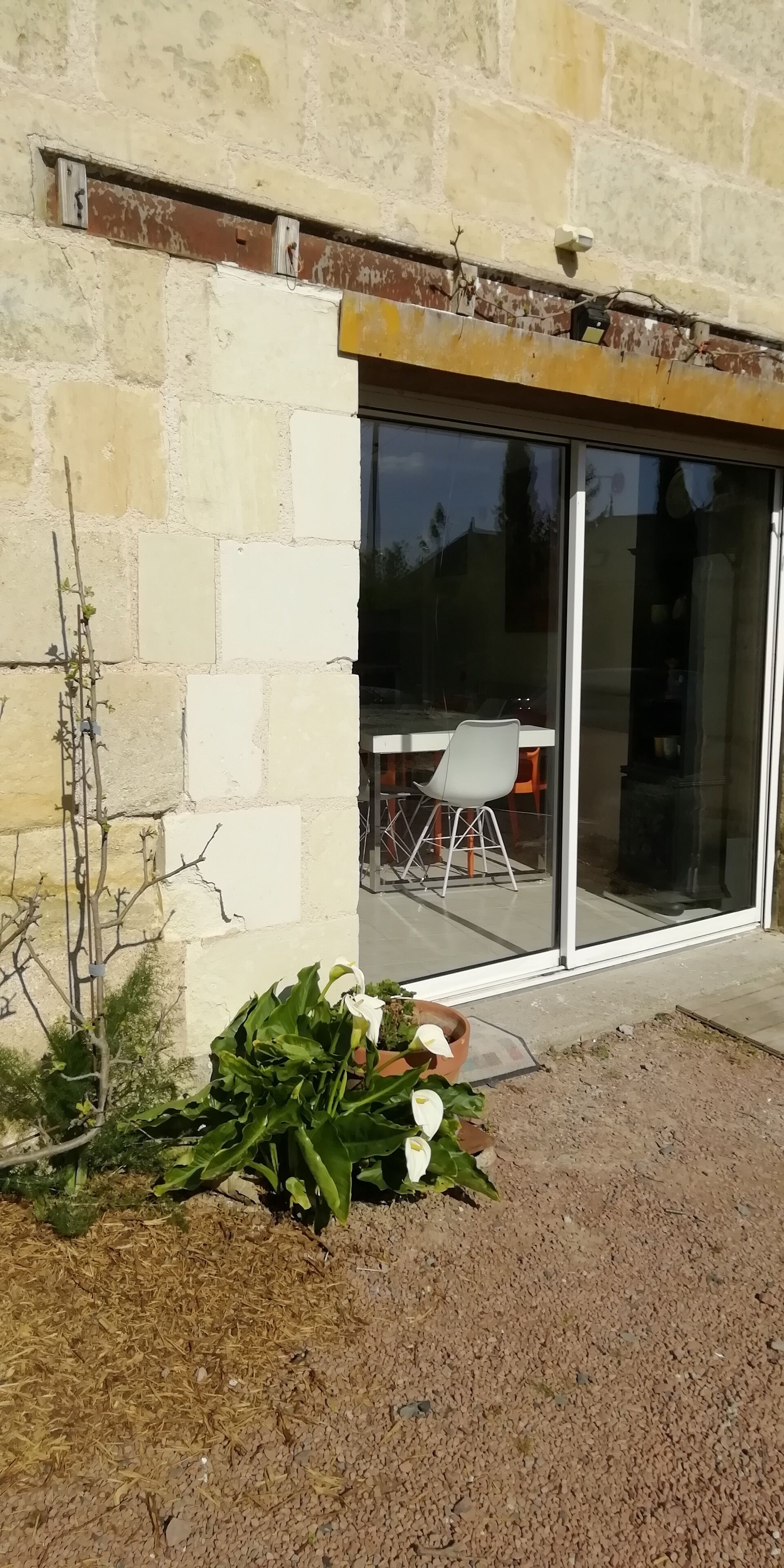 A building with a stone facade, a sliding glass door, and a small garden area with plants and a potted plant.
