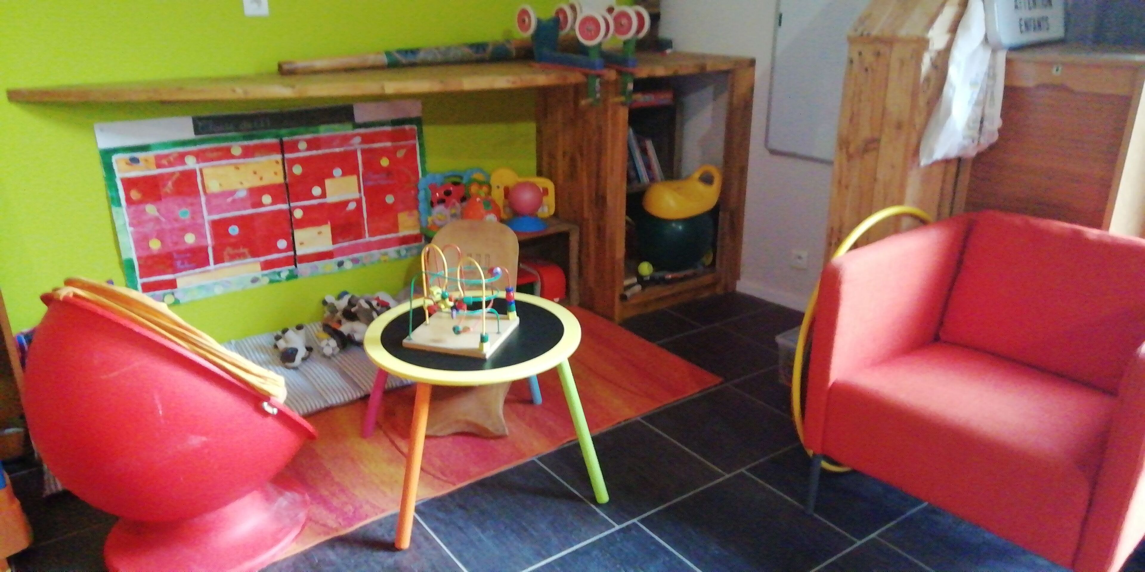 Una sala giochi con una sedia rossa, un tavolino e uno scaffale pieno di giocattoli.