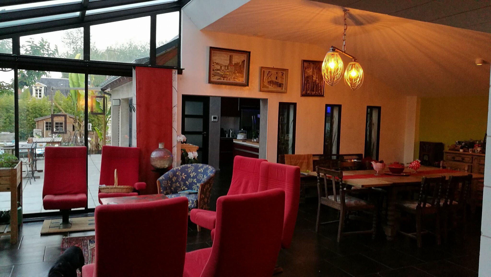 Un vaste espace de vie avec des fauteuils rouges, une table à manger et une cuisine en arrière-plan.