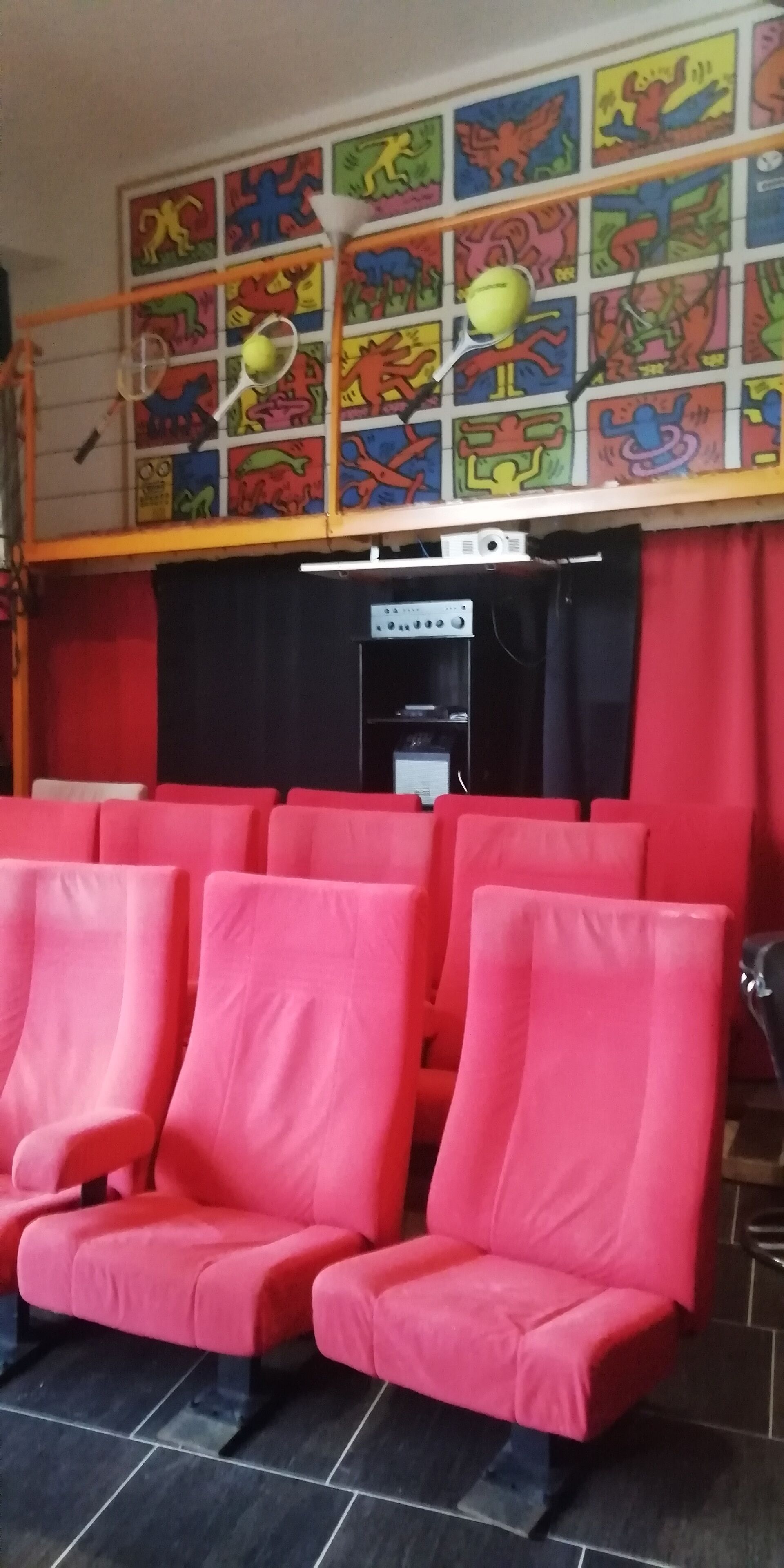 Una habitación con asientos rojos, una pantalla de proyector y coloridas obras de arte en las paredes.