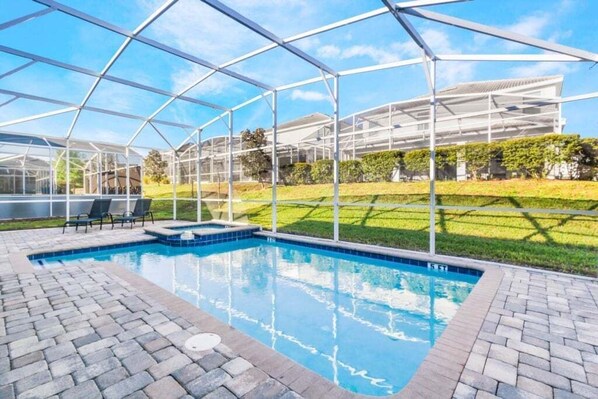 A swimming pool with a glass enclosure, surrounded by a brick patio and a grassy area.