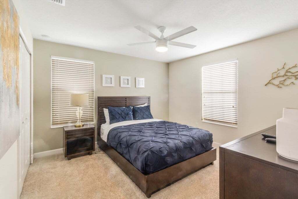 Un dormitorio con cama, mesitas de noche, ventilador de techo y persianas enrollables.
