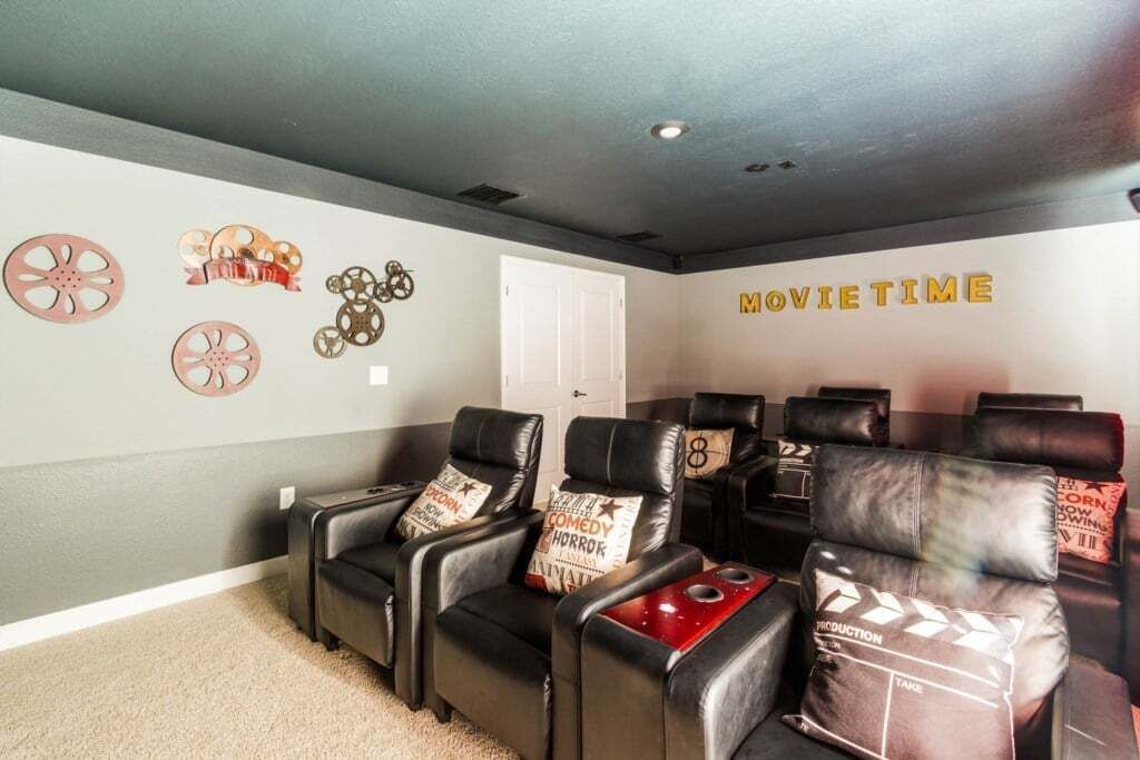 Une salle de cinéma privée avec des fauteuils inclinables en cuir noir, des coussins décorés sur le thème du pop-corn et un mur orné d’éléments rappelant le monde du cinéma.