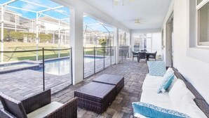 A covered outdoor patio with wicker furniture, a pool, and a glass-enclosed area. - Last Minute Disney! Private Pool, Hot Tub, Game Room & Themed Bedrooms. Book Now! #16282 (Orlando)