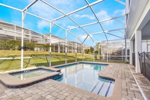 A pool area with a glass enclosure, a hot tub, and a brick patio.