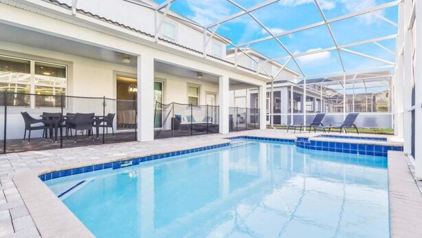 A pool area with a glass-enclosed structure, outdoor seating, and a clear blue sky. - Last Minute Disney! Private Pool, Hot Tub, Game Room & Themed Bedrooms. Book Now! #16282 (Orlando)