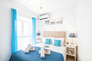 A hotel room with a bed, two bedside tables, a nightstand, a window with curtains, and wall-mounted air conditioning. - Cozy House in Albufeira, by the Beach (Albufeira)