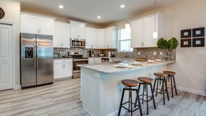 Una cocina moderna con armarios blancos, una isla grande con taburetes, electrodomésticos de acero inoxidable y un piso con patrón de espiga.
