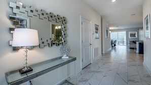 Un couloir avec une console en verre, un miroir mural moderne et une porte donnant sur une autre pièce.